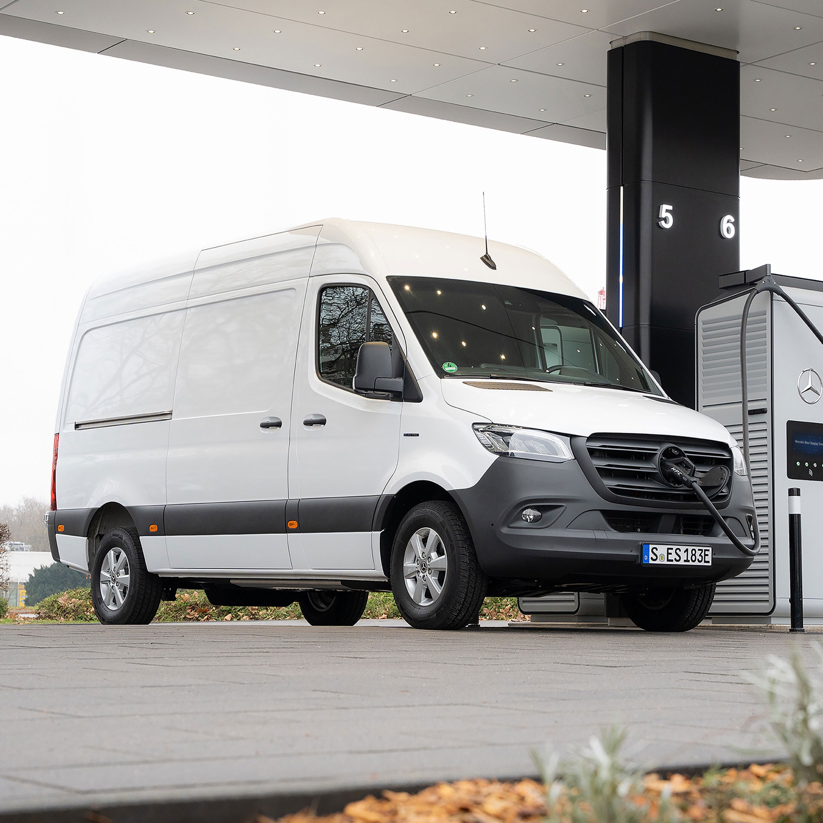 Ein weißer Sprinter Kastenwagen, wird an einer E-Ladesäule auf einem Parkplatz geladen.