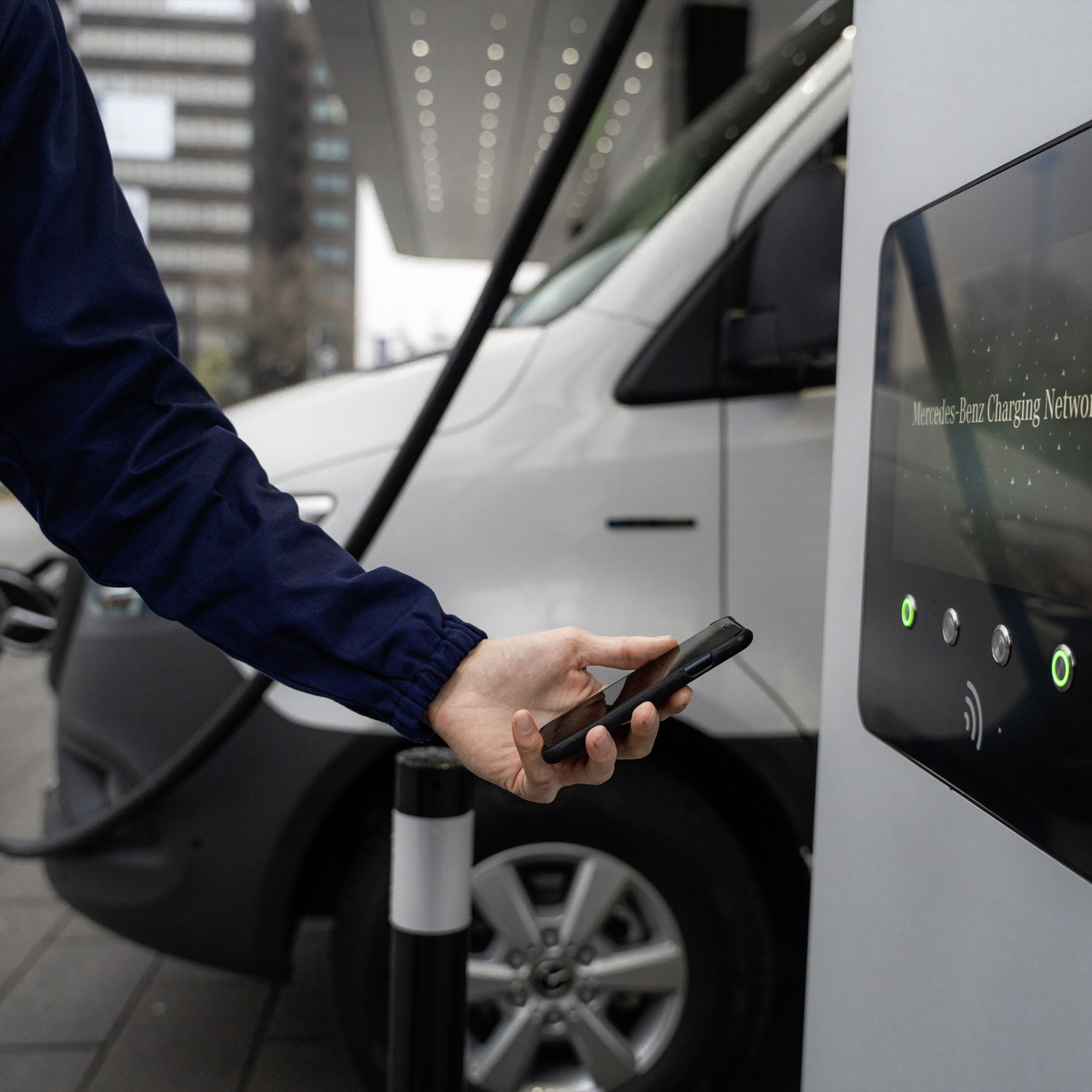 Ein Mann hält sein Smartphone zum Zahlen des Ladevorgangs an die Ladesäule.