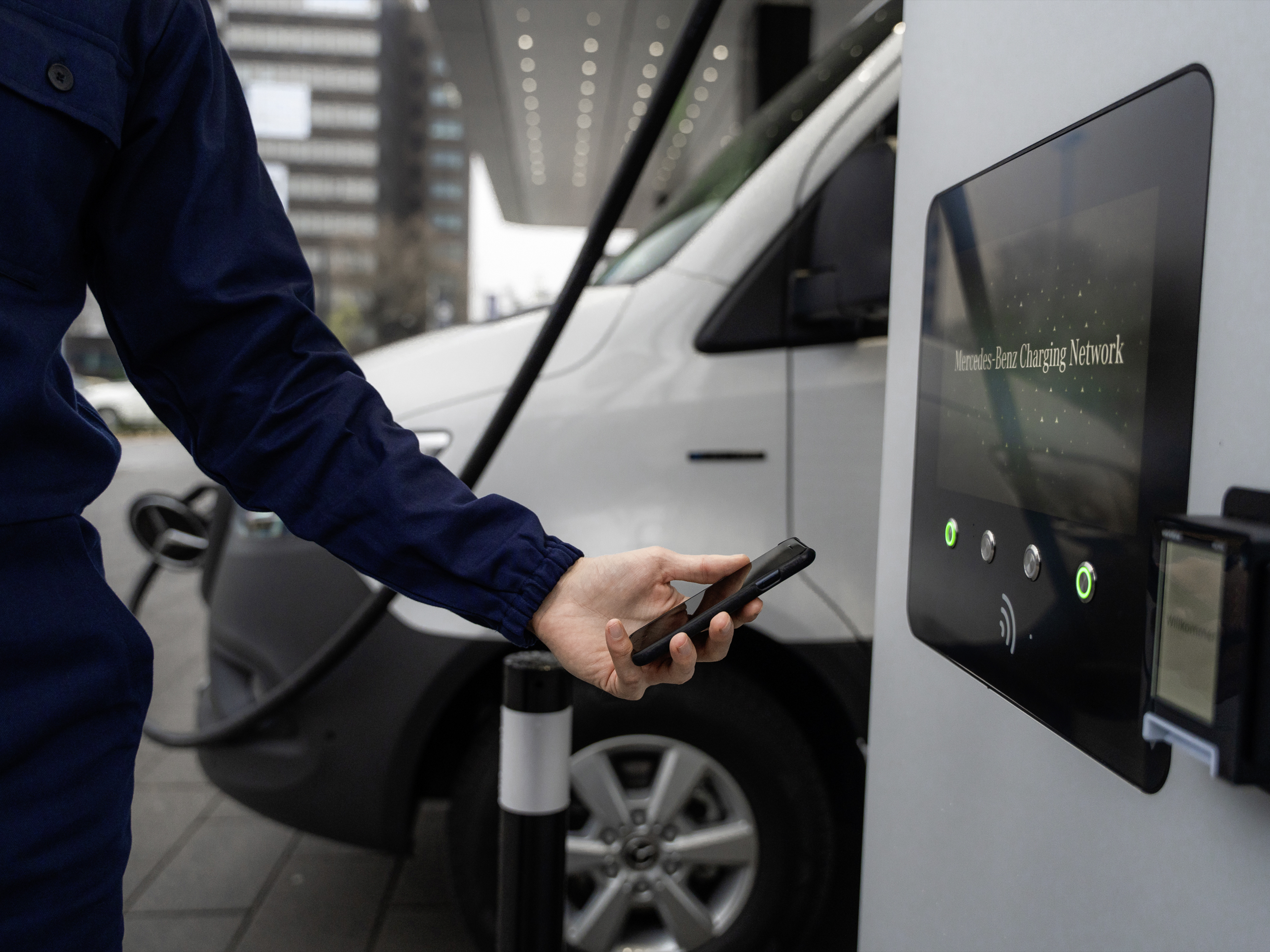Laden untewegs | Mercedes-Benz Transporter. Ein Mann hält sein Smartphone zum Zahlen des Ladevorgangs an die Ladesäule.