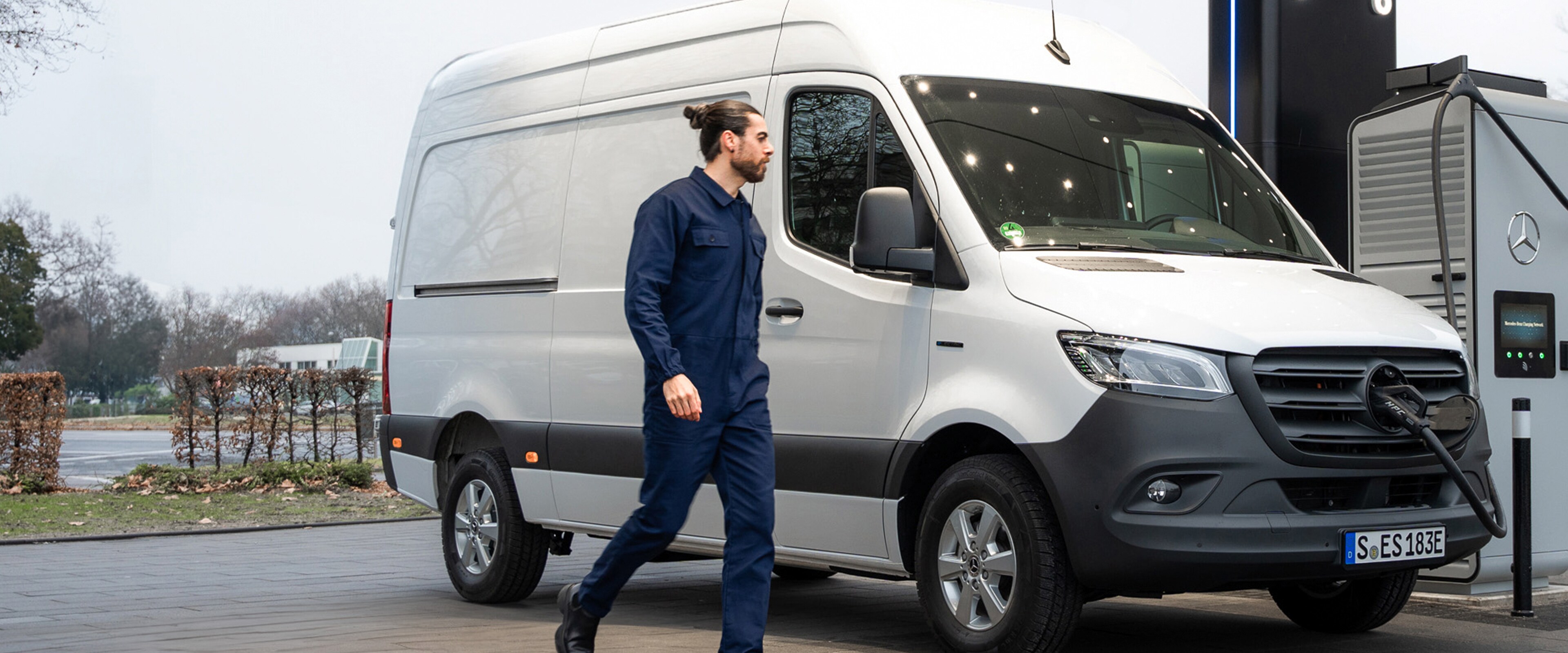 Ein Mann geht zu einem Mercedes-Benz Transporter, der an einer öffentlichen Ladesäule parkt.
