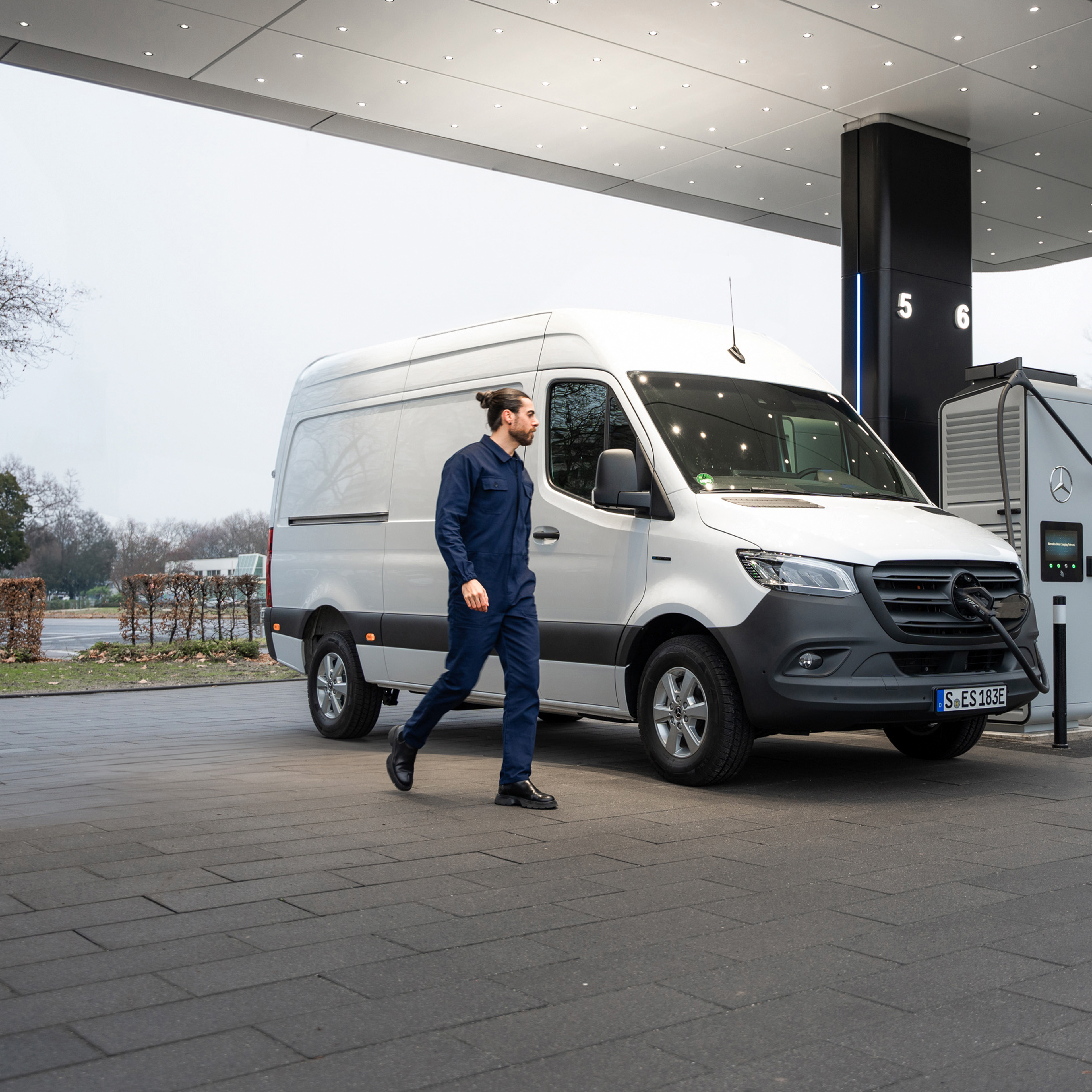 Laden unterwegs | Mercedes-Benz Tansporter. Ein Mann geht zu einem Mercedes-Benz Transporter, der an einer öffentlichen Ladesäule parkt.