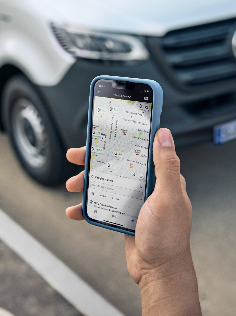 Eine Person hält ein Smartphone in den Händen, das die Funktionen von Mercedes-Benz MBUX zeigt. Ein Transporter steht im Hintergrund.