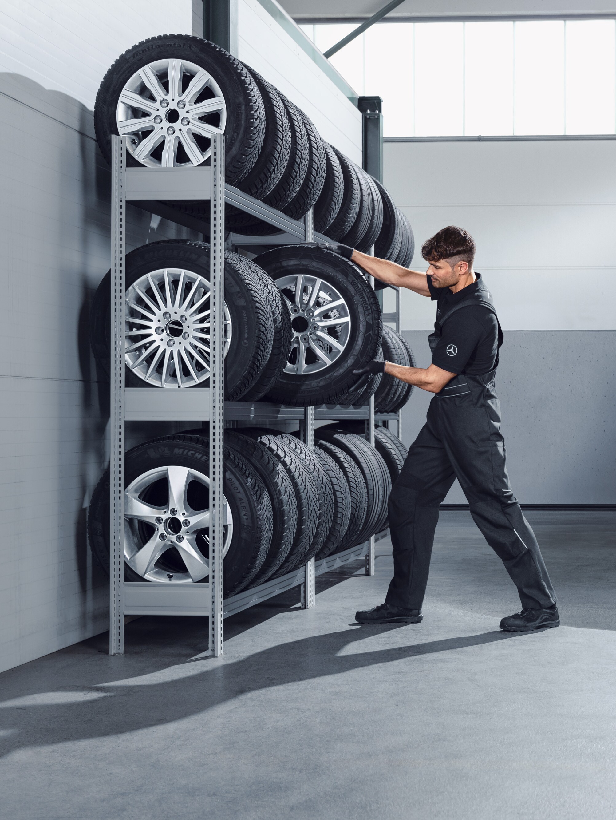 Mechaniker wählt Mercedes-Benz Winterkompletträder für einen weißen Sprinter aus dem Regal in der Werkstatt.