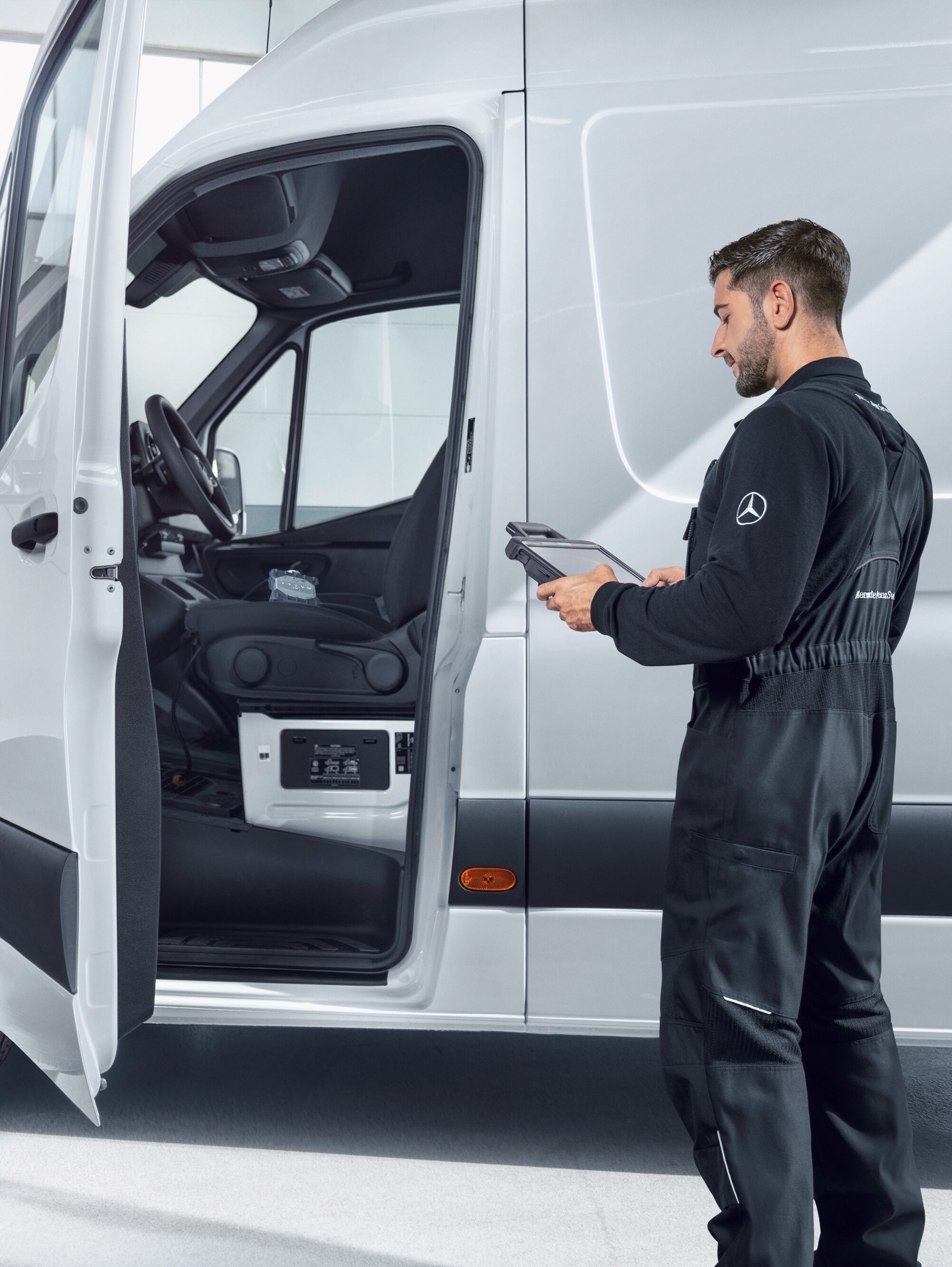 Mechaniker mit Tablet prüft weißen Mercedes-Benz Transporter, Symbol für Qualitätsstandards und Qualitätsversprechen.