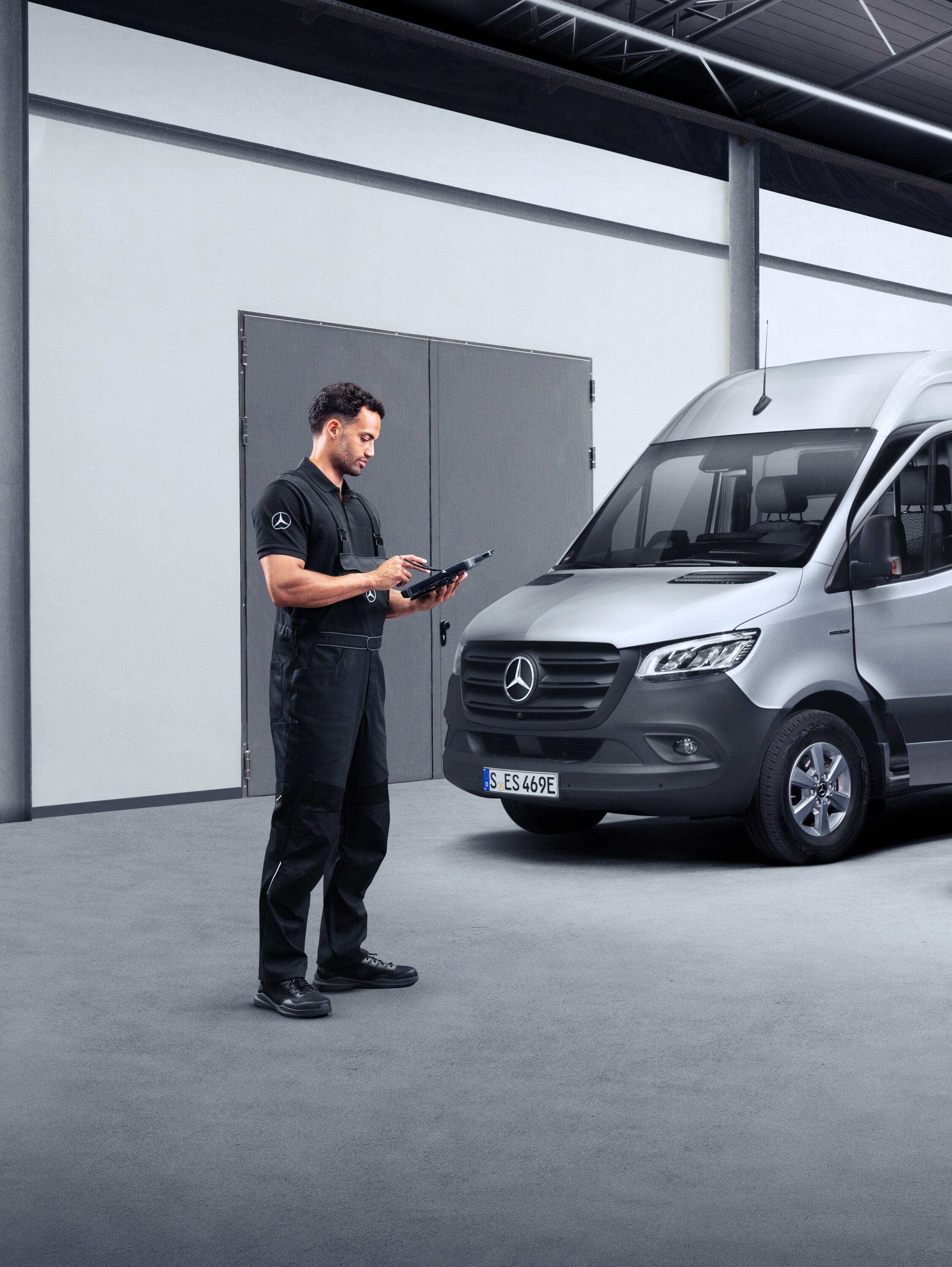 Ein Techniker steht vor Mercedes-Benz Transportern in einer Halle – abgesichert mit dem Mercedes Service Paket.