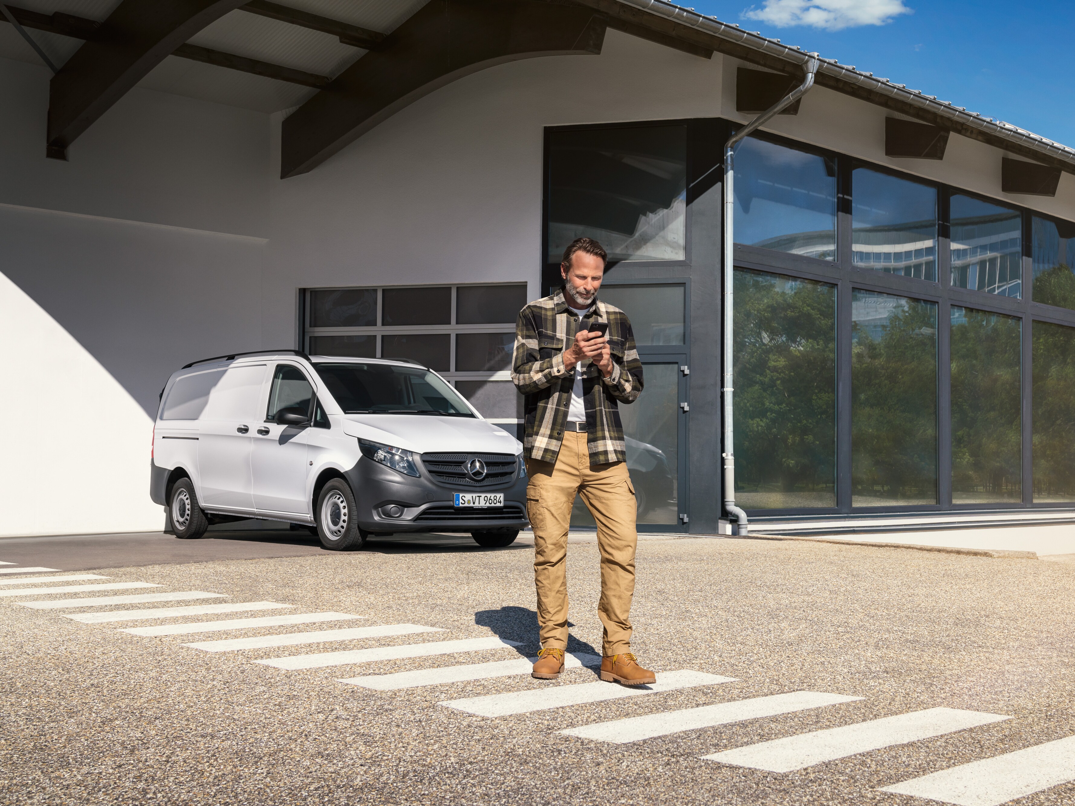 Ein Mann steht vor einem weißen Mercedes-Benz Vito und benutzt sein Smartphone.