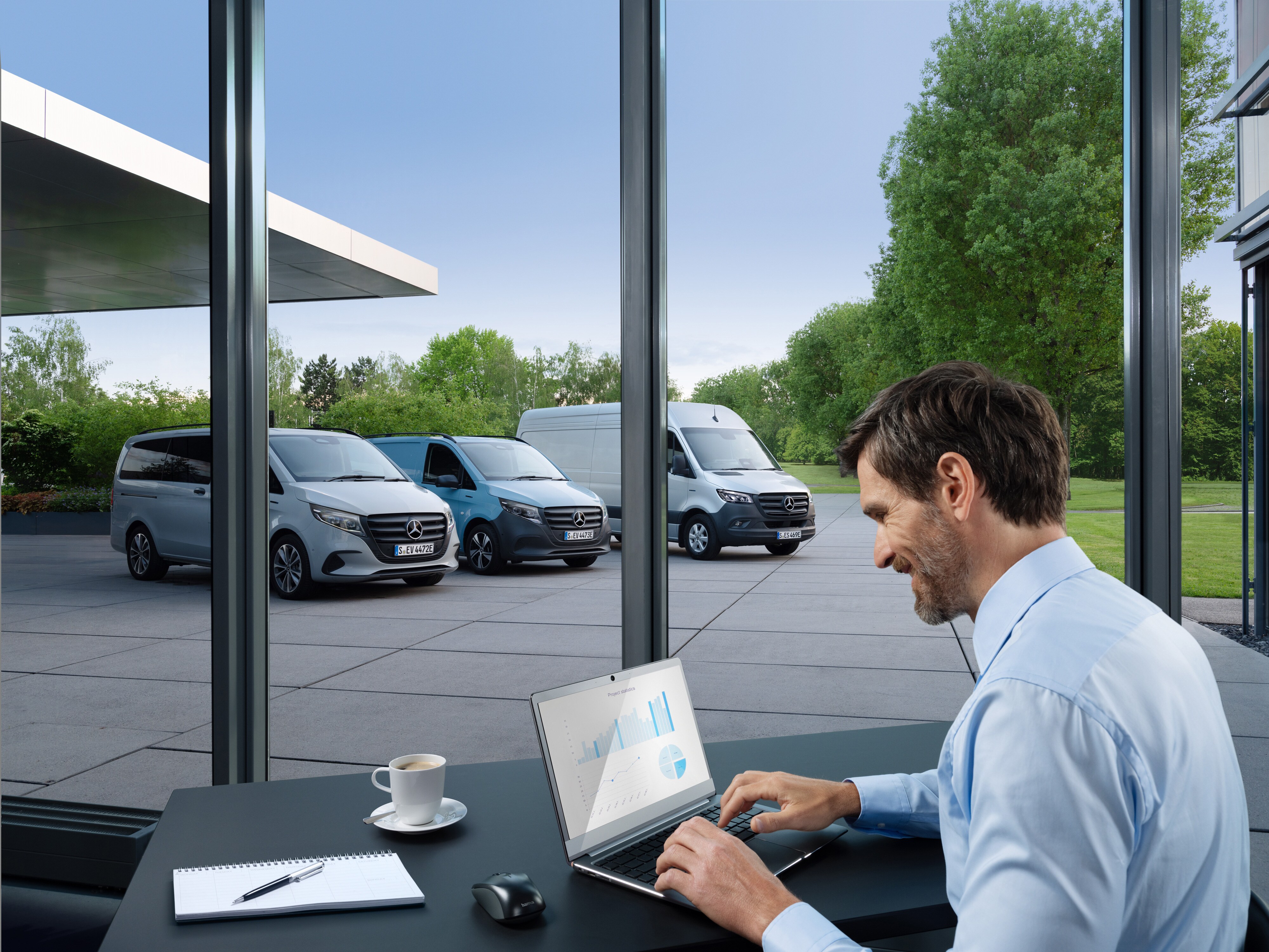 Ein Mann arbeitet an einem Laptop, draußen steht eine Reihe von Mercedes-Benz Transportern.