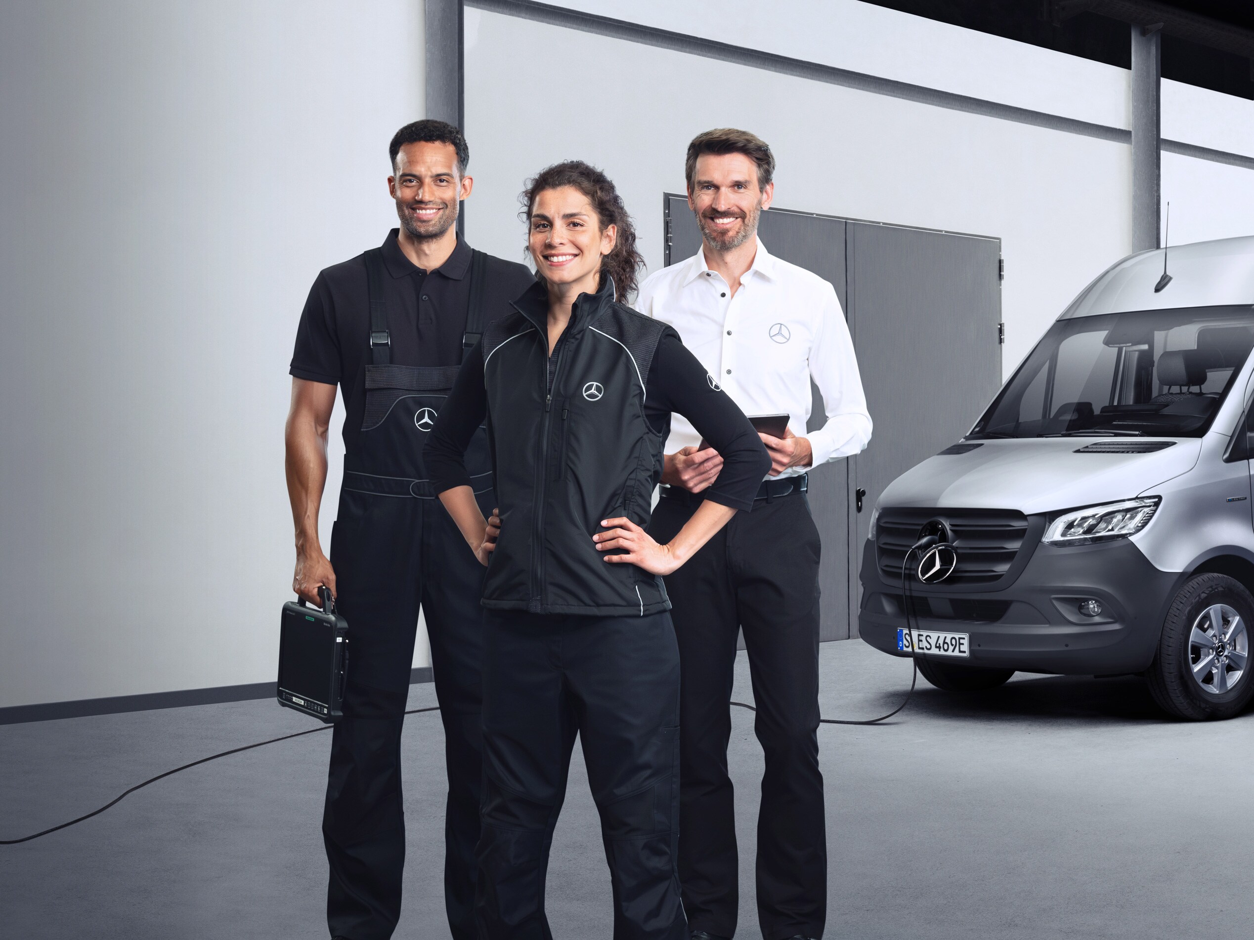 Drei Mitarbeiter vor einem elektrischen Mercedes-Benz Sprinter mit angeschlossenem Ladekabel.