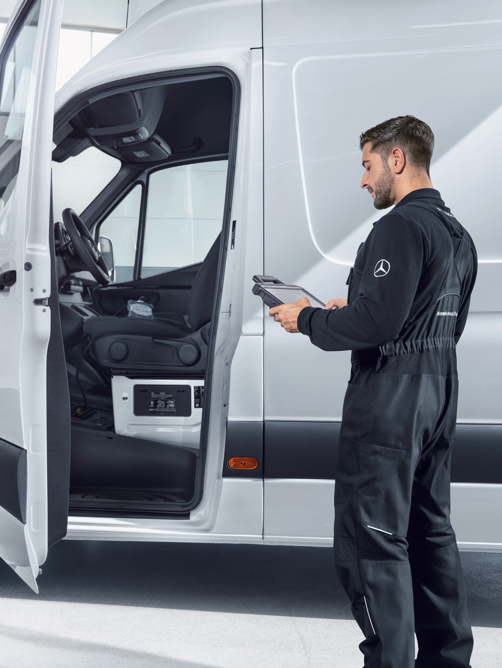 Ein Techniker im Overall überprüft einen weißen Mercedes-Benz Sprinter mit einem Tablet.