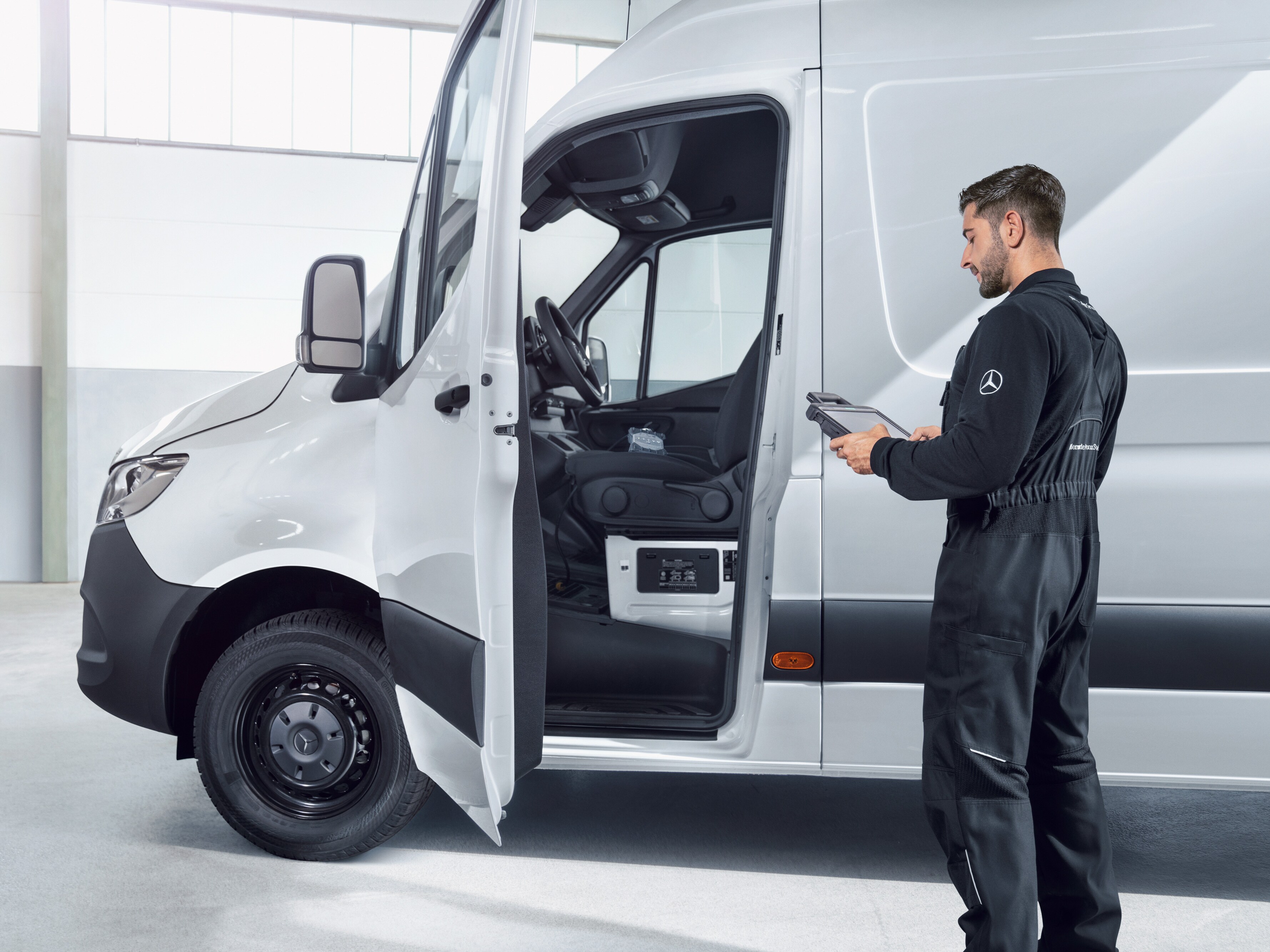 Ein Techniker im Overall überprüft einen weißen Mercedes-Benz Sprinter mit einem Tablet.