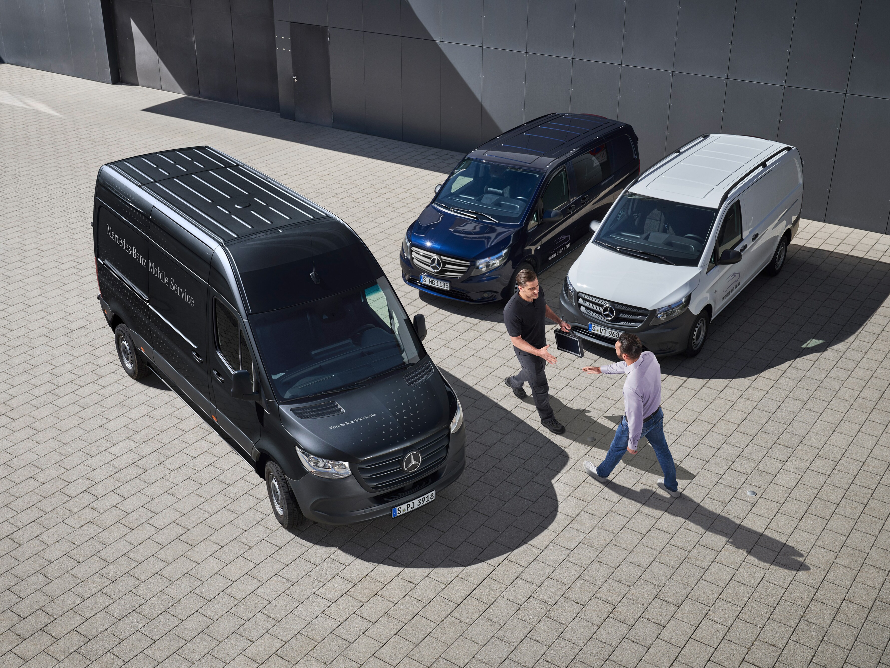 Ein Kundenberater von Mercedes-Benz begrüßt einen Kunden auf einem Parkplatz auf dem drei Mercedes-Benz Transportern stehen.