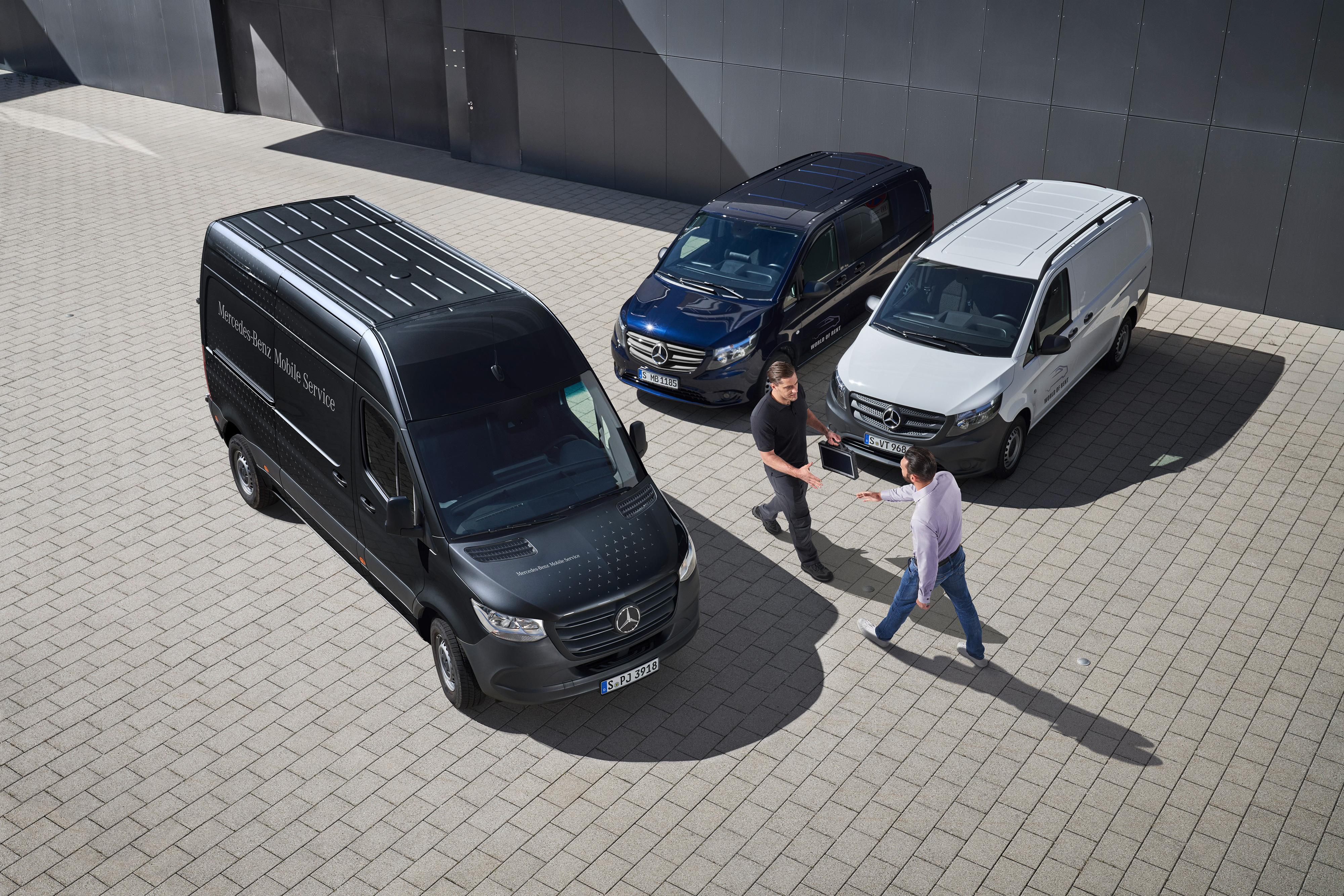 Fleet Services | Mercedes-Benz Transporter. Ein Kundenberater von Mercedes-Benz begrüßt einen Kunden auf einem Parkplatz auf dem drei Mercedes-Benz Transportern stehen.