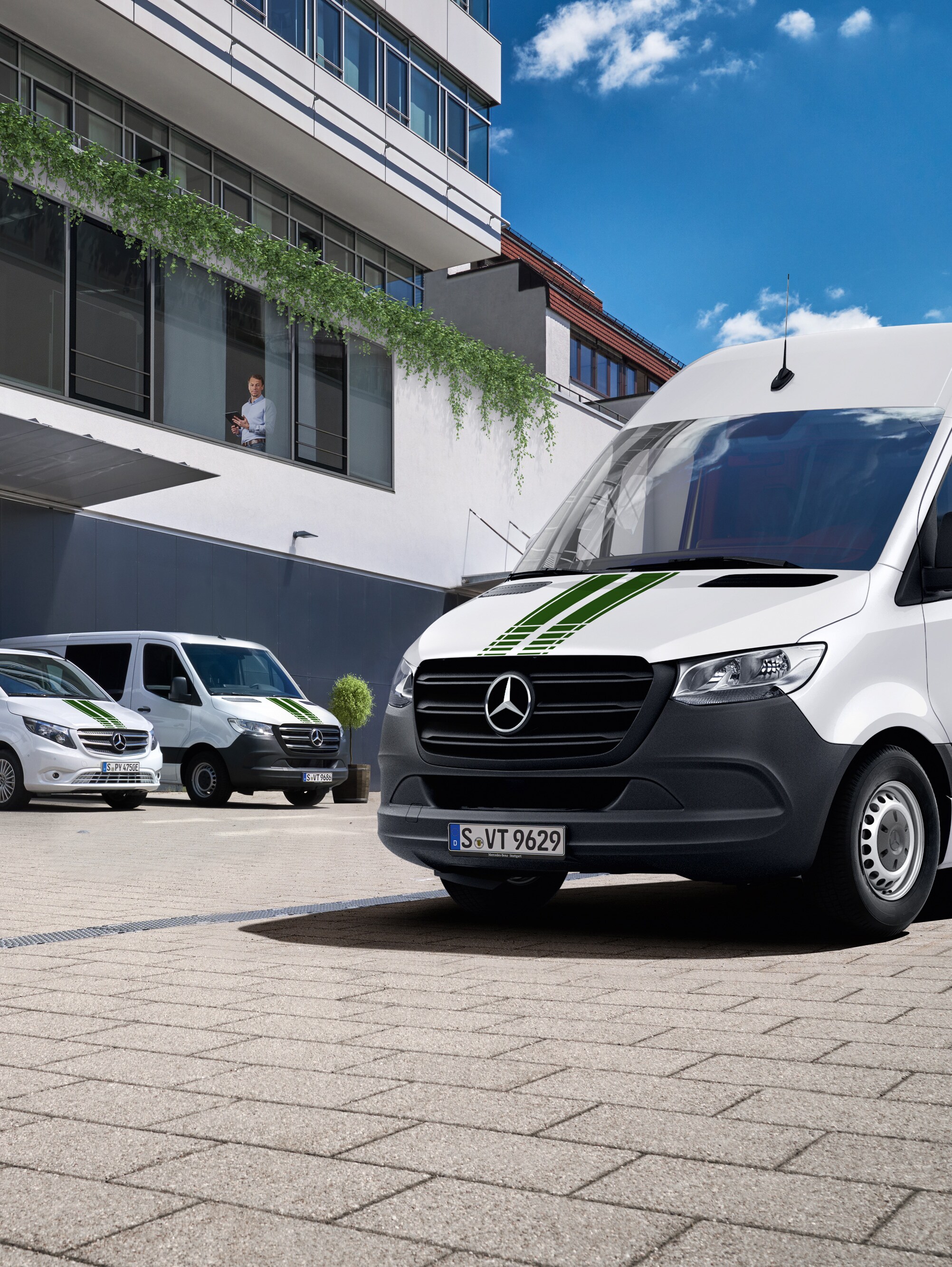 Eine Flotte weißer Mercedes-Benz Transporter vor einem Bürogebäude an einem sonnigen Tag mit blauem Himmel.