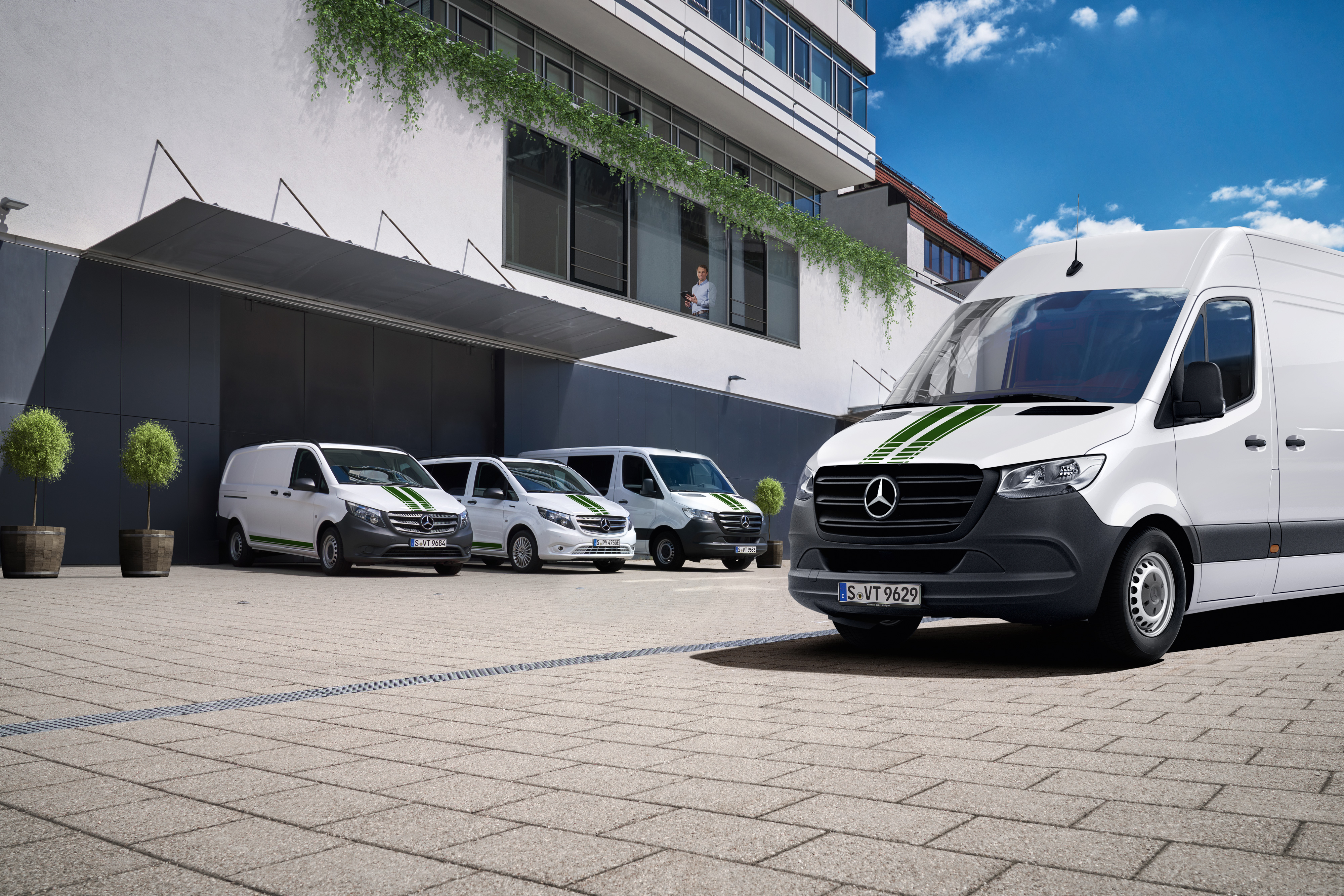 Fleet Services | Mercedes-Benz Transporter. Eine Flotte weißer Mercedes-Benz Transporter vor einem Bürogebäude an einem sonnigen Tag mit blauem Himmel.