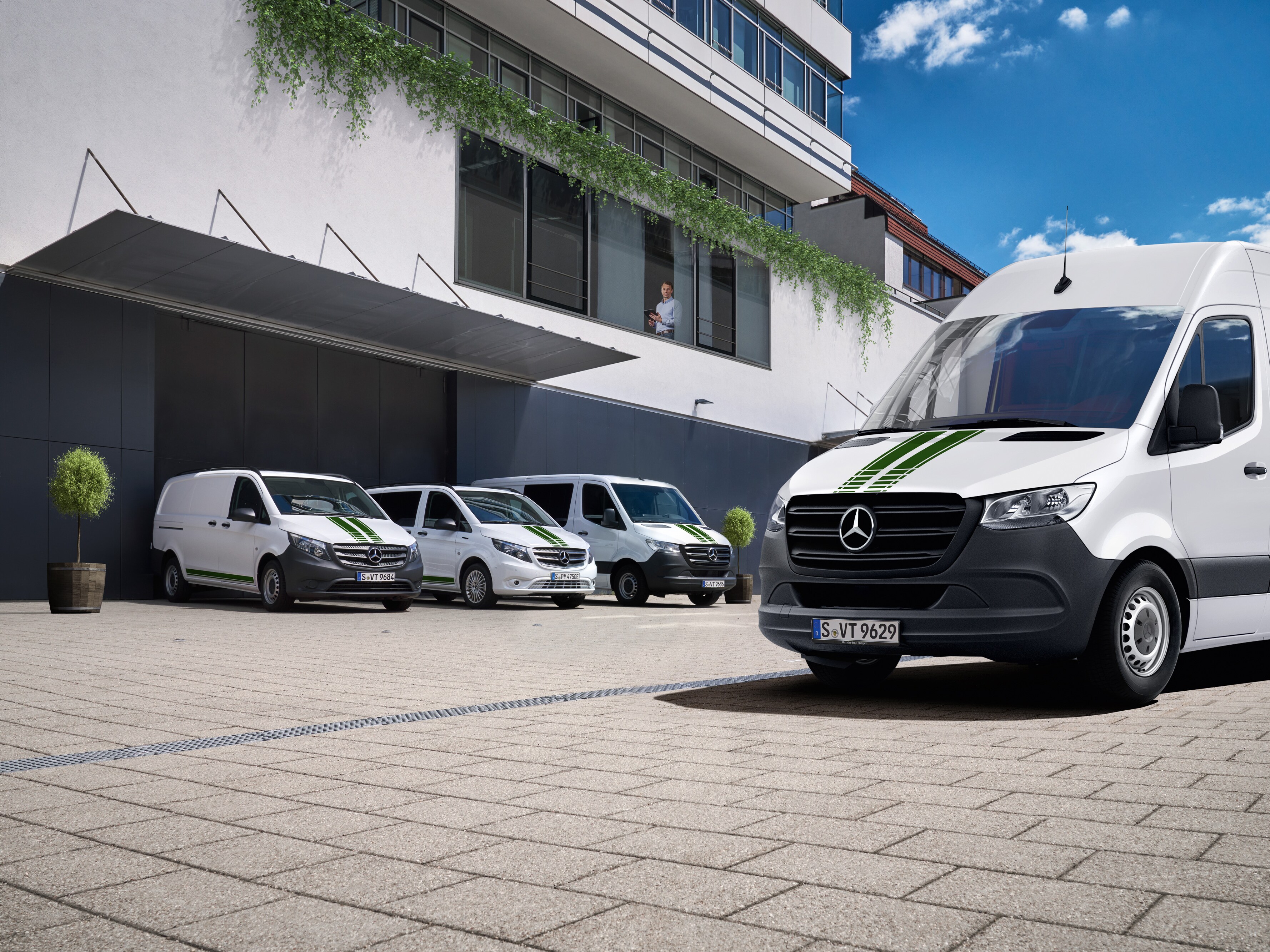 Eine Flotte weißer Mercedes-Benz Transporter vor einem Bürogebäude an einem sonnigen Tag mit blauem Himmel.