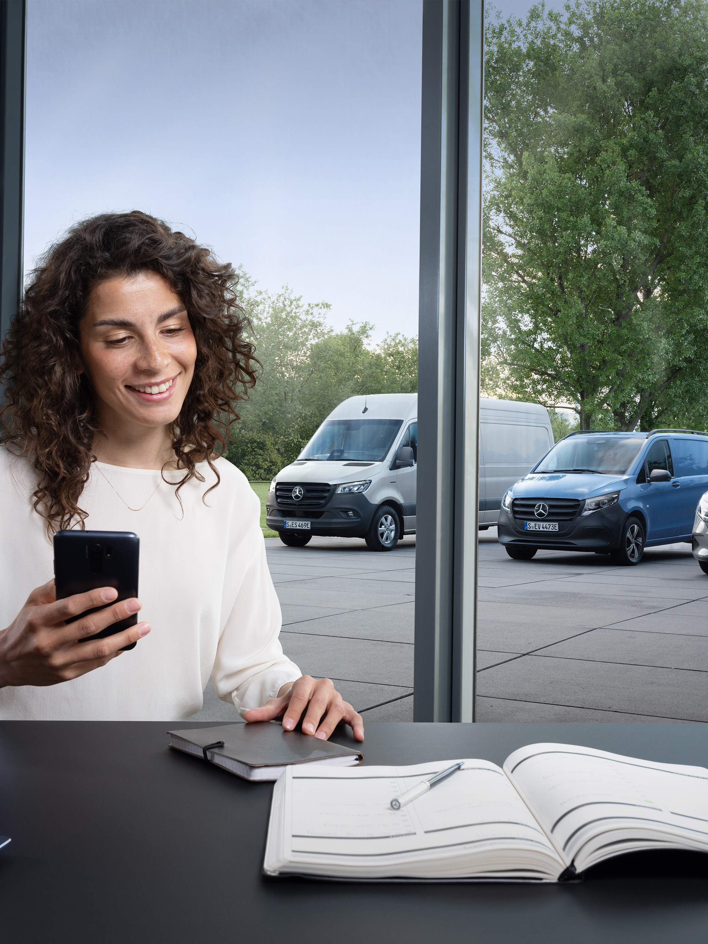 Frau plant am Smartphone vor Mercedes-Benz Vans – optimal betreut mit dem Mercedes Service Paket.