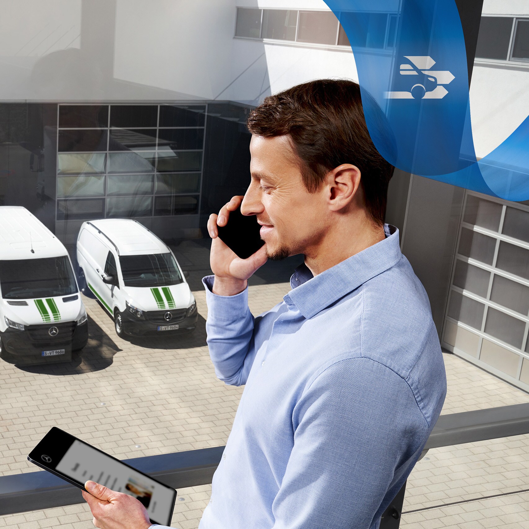 Ein Mann telefoniert, während er auf ein Tablet schaut, mit einer Reihe von Mercedes-Benz Transportern im Hintergrund.