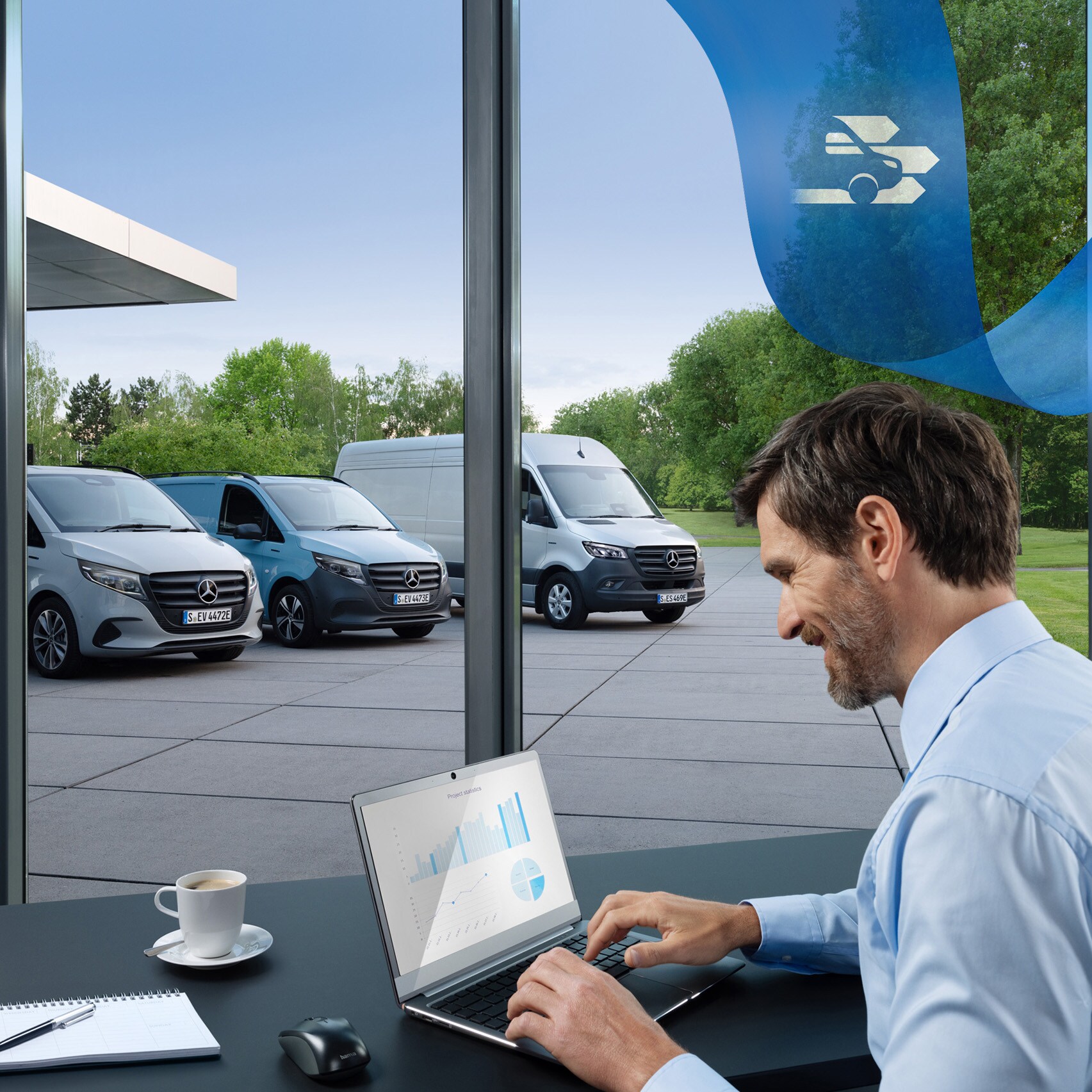 Ein Mann arbeitet mit einem Laptop in einem Büro mit einer Reihe von Mercedes-Benz Transportern im Hintergrund.