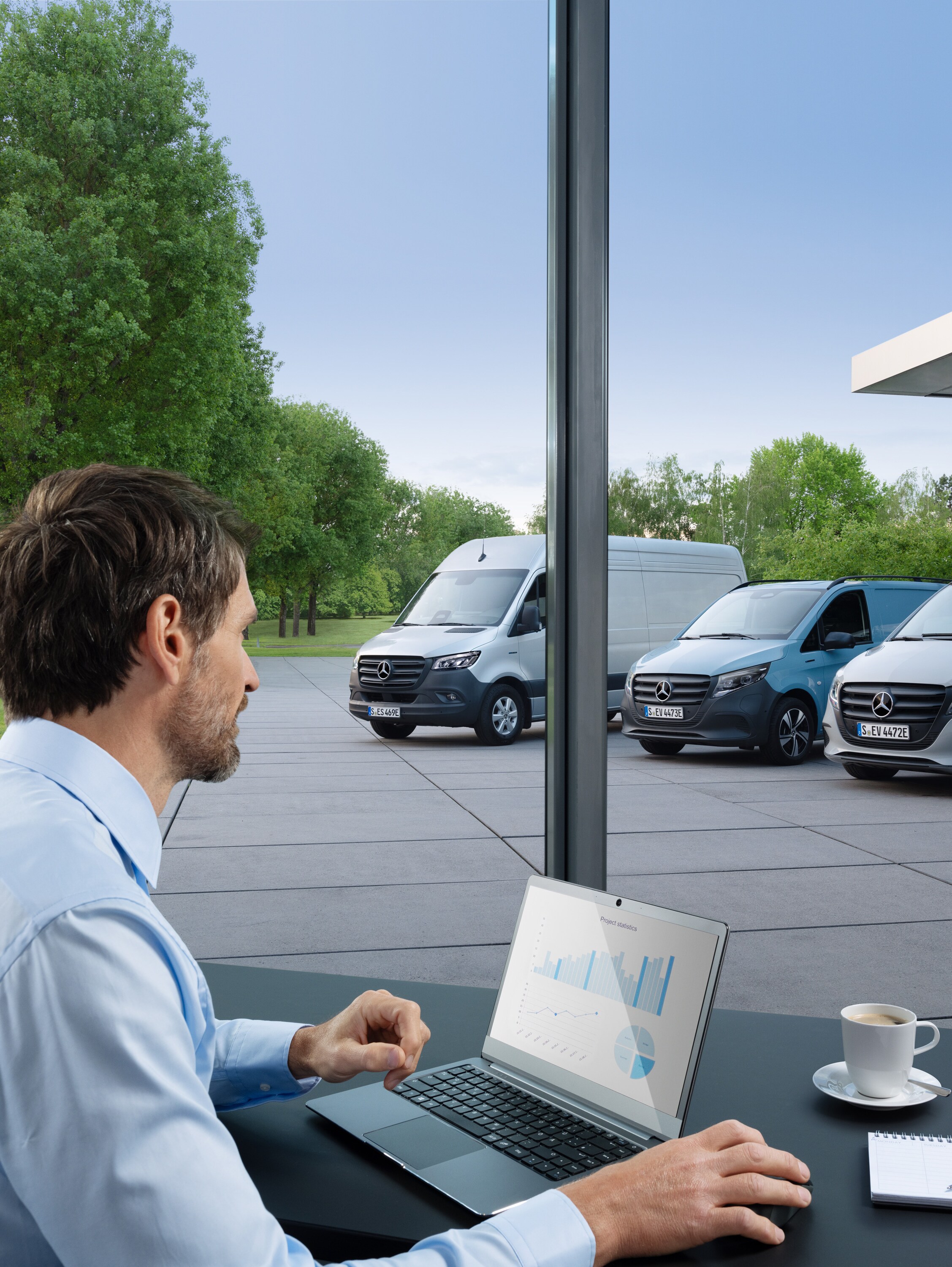 Ein Mann überwacht mehrere geparkte Mercedes-Benz Transporter mit einem Laptop, Symbol für digitales Fuhrparkmanagement.