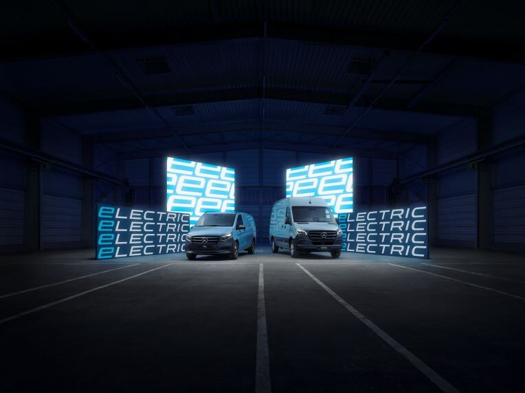 Zwei Transporter von Mercedes-Benz auf einer Straße vor leuchtenden Tafeln und abgedunkeltem Hintergrund.