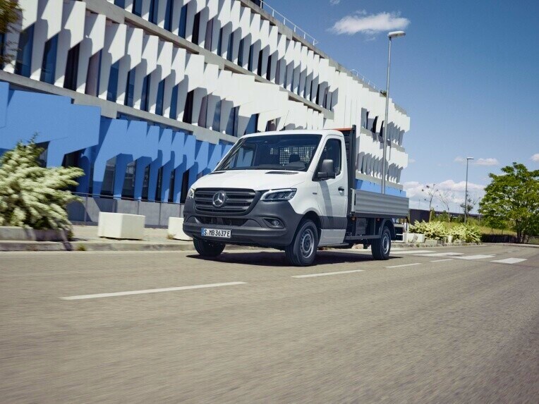 Das Mercedes-Benz eSprinter Fahrgestell im Straßenverkehr vor einem weiß-blauen Gebäude.