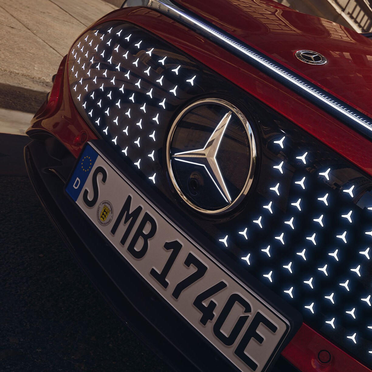 Die neue vollelektrische CLA Limousine in rot mit beleuchtetem Frontdesign und Sternen Pattern.