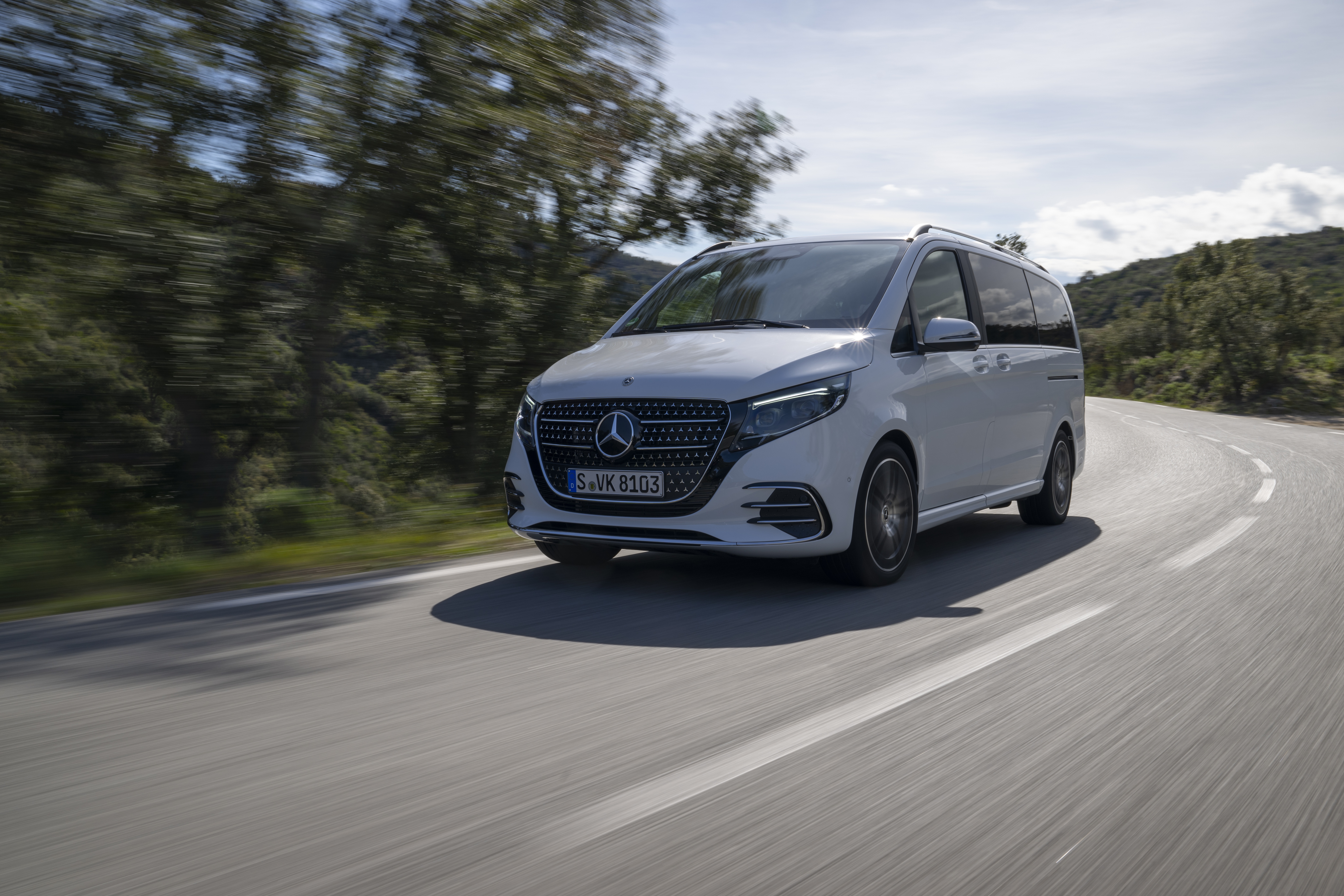 T-Klasse | Discontinued | Mercedes-Benz. Eine weiße V-Klasse von Mercedes-Benz fährt auf einer sonnigen Landstraße an Bäumen entlang.